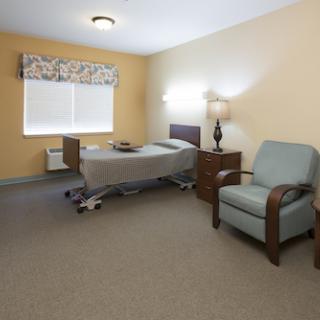 A spacious, well-lit hospital room featuring a bed, chair, and natural light from the window.