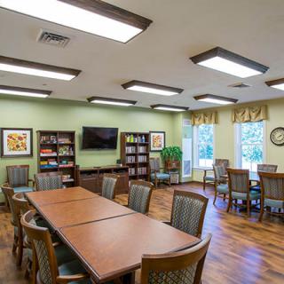 A well-lit meeting room with tables, chairs, bookshelves, and a television.