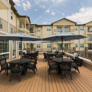 A spacious outdoor patio with tables, chairs, and umbrellas in front of an apartment building.