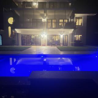 A modern house illuminated at night with a glowing pool in the foreground.