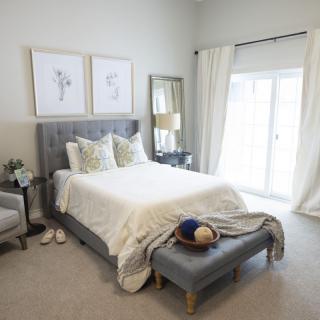 A modern and bright bedroom featuring a comfortable bed with plush pillows, neutral decor, and large windows with sheer curtains.