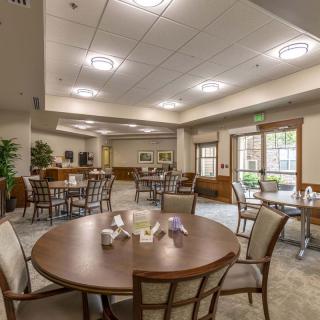 A modern dining area with round tables and chairs, featuring ample lighting and large windows.