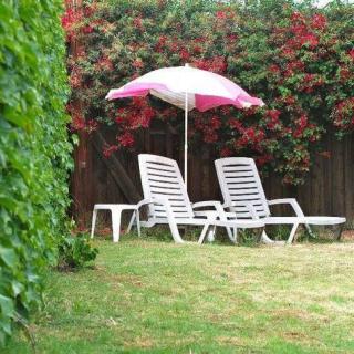A serene garden setting with two lounge chairs and a pink umbrella amidst lush greenery and blooming flowers.