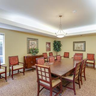 A spacious meeting room featuring a large wooden table surrounded by comfortable red chairs, adorned with artwork and complemented by indoor plants.