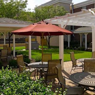 A charming outdoor patio with a red umbrella and comfortable seating surrounded by lush greenery.