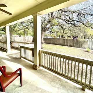 A sunny porch with a red chair overlooking a fenced yard and trees.