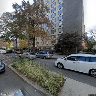 A busy urban street lined with cars, trees, and a tall residential building on an autumn day.