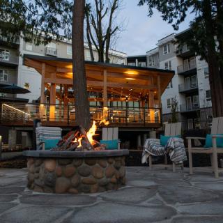 A cozy outdoor seating area with a fire pit in front of a well-lit building in the evening.