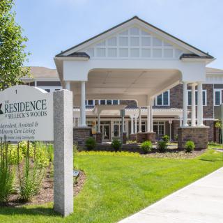 The image shows the entrance of a residential building with well-maintained landscaping and clear signage.