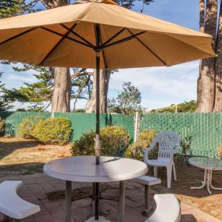 A cozy outdoor patio area with a round table, umbrella, and chairs surrounded by greenery.