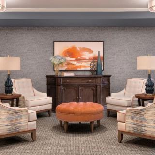 A cozy lounge area with plush chairs, an orange ottoman, and decorative lamps.