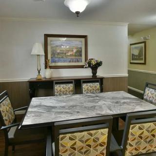 A cozy dining room with a marble-topped table and patterned chairs, adorned with a painting, lamp, and vase.