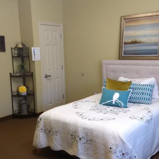 A cozy bedroom featuring a neatly made bed with colorful pillows, a wall painting, and shelves for decoration.