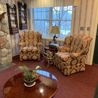 A cozy living room with patterned armchairs, a wooden table with a potted plant, and a lamp near the window.