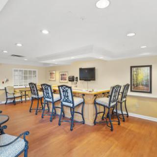 A cozy bar area featuring high chairs, a large counter, and a television, set against warm wooden flooring.