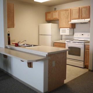 A compact apartment kitchen with wooden cabinets, a refrigerator, stove, and countertop.