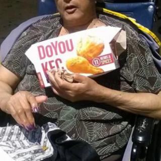 A woman in a wheelchair holding a box of fried chicken.
