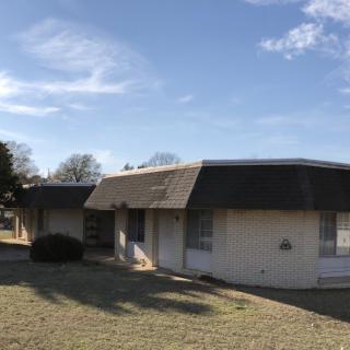 A single-story suburban house with a manicured lawn under a clear blue sky.