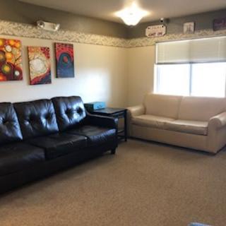 A cozy living room featuring a black and a beige sofa, decorated with colorful artwork on the walls.