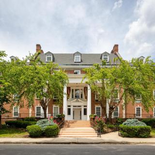 A grand colonial-style building with a symmetric faade, large columns, and surrounded by lush green trees.