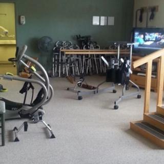 A rehabilitation room equipped with various physical therapy tools including a stationary bike, walkers, and parallel bars.