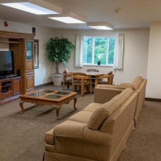 A cozy living room featuring a sofa, coffee table, and entertainment center with a television. A dining table is set near the window, complemented by an indoor plant.