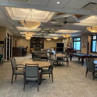 A spacious and well-lit recreation room with multiple tables and chairs arranged for social gatherings.