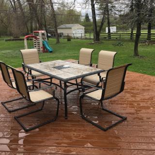 A set of outdoor furniture consisting of a table and chairs on a wet wooden deck in a backyard.