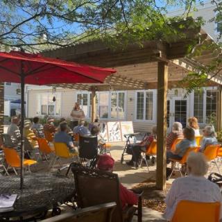 A sunny outdoor event with an audience seated under a canopy.