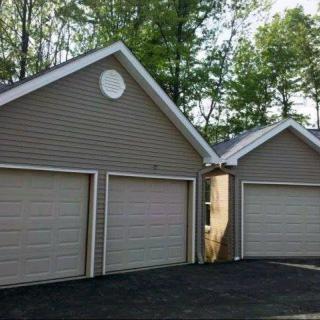 Three attached garage units with a shared driveway and surrounded by trees.