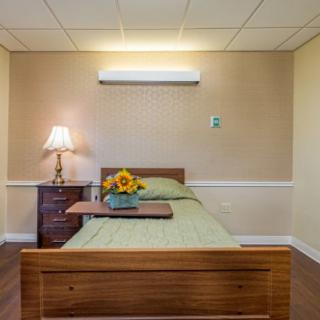 A minimalist bedroom with a single wooden bed, bedside table with a lamp, and a decorative flower vase.