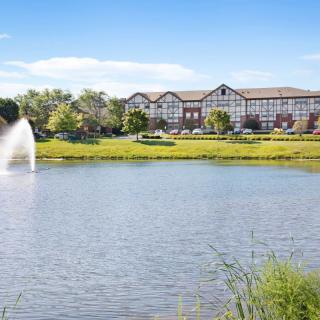 A scenic view of a building by the lake with a fountain and lush greenery.