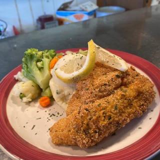 A plate of crispy fried chicken served with mashed potatoes, steamed broccoli, and carrots, garnished with a slice of lemon.