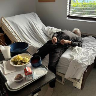 A patient lying in a hospital bed with a meal tray nearby.