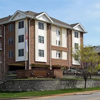A modern residential apartment building featuring a brick facade and multiple stories, surrounded by greenery.