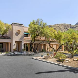 A house with a desert landscape, surrounded by trees and mountains in the background.