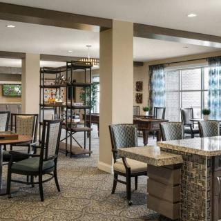 A modern dining area with tables, chairs, and soft carpeted flooring, featuring natural lighting and contemporary decor.