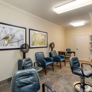 A hair salon waiting area with chairs and hair dryers, featuring framed artwork on the walls.