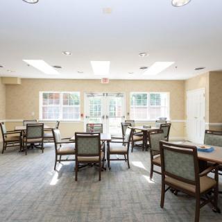 A bright and spacious dining room with several tables and chairs, illuminated by natural light from large windows.