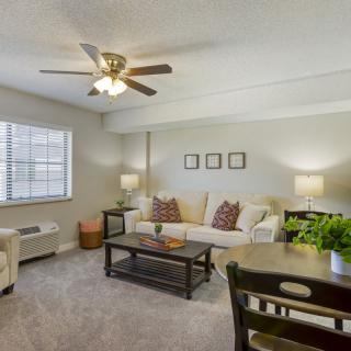 A cozy living room with neutral tones, featuring a sofa, coffee table, ceiling fan, and stylish decor.