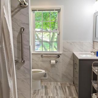 A modern bathroom with a shower, toilet, and sink, featuring marble tiles and a large window.