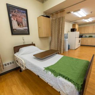 A clean and organized hospital room with a single bed and kitchenette.