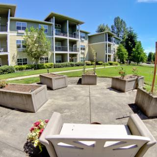 A serene outdoor space with benches and planters, surrounded by a well-maintained apartment complex.