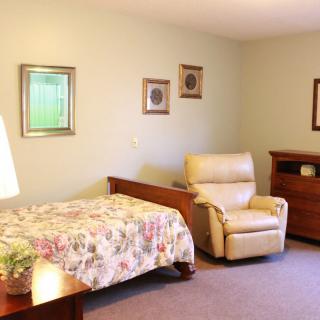 A cozy bedroom featuring a bed with floral bedding, an armchair, framed wall art, and a lamp.