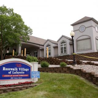 Exterior view of a senior living facility with a welcoming sign and landscaped surroundings.