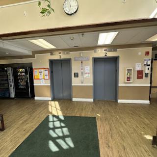 A spacious lobby featuring elevators, a clock, and a vending machine.
