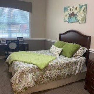 A cozy bedroom featuring a bed with green accent pillows and a decorative painting above the headboard.