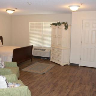 A cozy bedroom with a wooden floor, featuring a bed, dresser, and armchairs.
