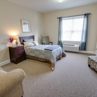 A cozy bedroom with a single bed, large window, and comfortable seating area.