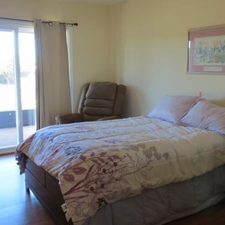 A cozy bedroom with a large bed, an armchair by the window, and artwork on the wall.